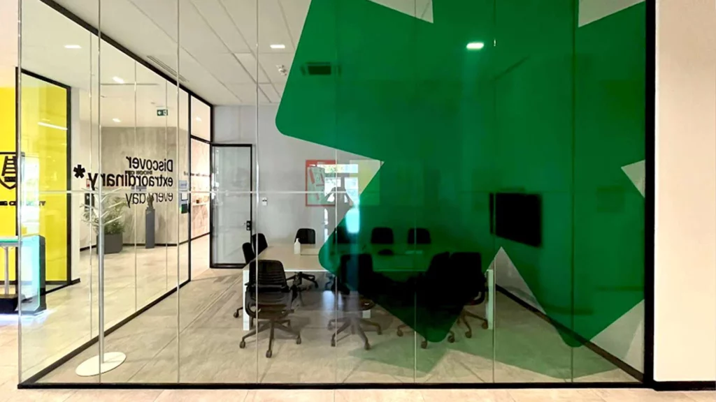 Sala riunioni moderna visibile attraverso pareti di vetro decorate con pellicola adesiva verde a forma geometrica, con la scritta in vinile smerigliato "Discover Extraordinary" su una porta in vetro, ideale per insegne luminose da interno.