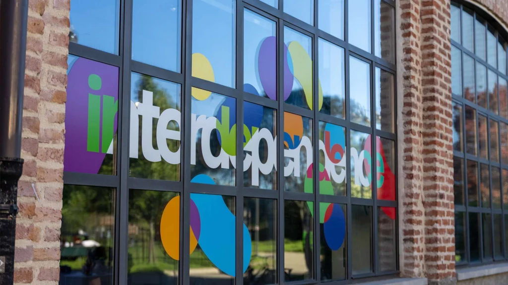 Vetrata con grafica colorata e scritta in vinile bianco "Il Telerappresentato" su sfondo di cerchi colorati, affissa sulla facciata in mattoni di un edificio, ideale per insegne luminose da esterno.