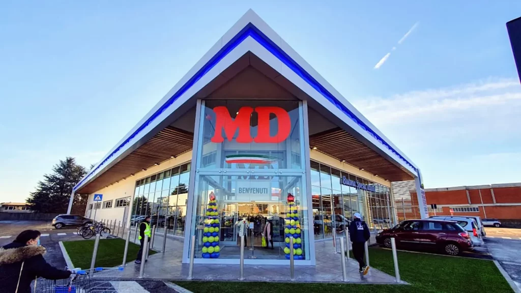 Facciata di un punto vendita MD Supermercati con il logo MD rosso e la bandiera italiana in un atrio di vetro, ideale per insegne luminose da esterno.