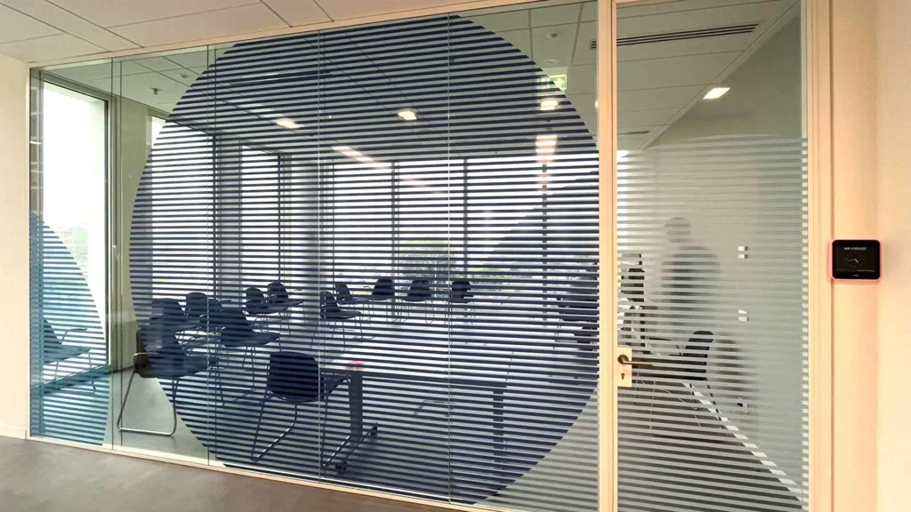 Sala riunioni moderna con pareti vetrate, decorate con grande pellicola adesiva a cerchio a righe orizzontali blu e grigie, ideale per insegne luminose da interno.