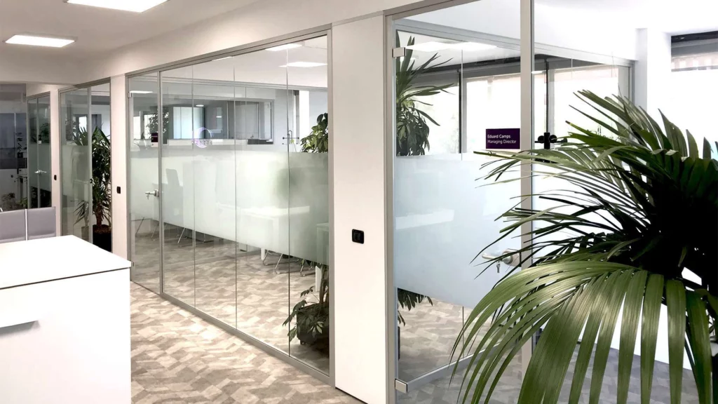 Ufficio moderno con pareti divisorie in vetro decorate con strisce orizzontali in pellicola adesiva smerigliata per la privacy e piante verdi, ideale per insegne luminose da interno.