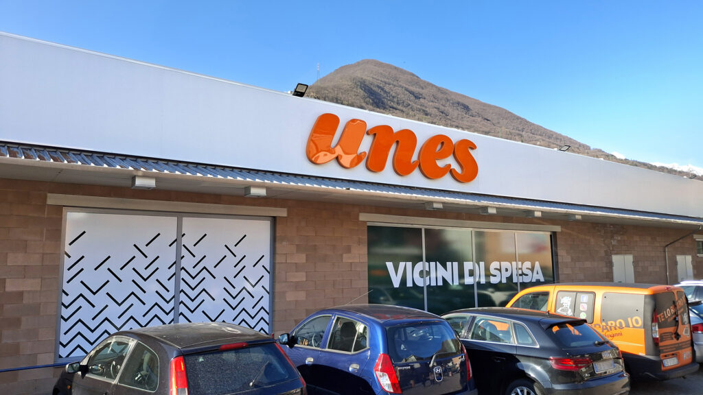 Insegna luminosa Unes arancione sulla facciata di un supermercato