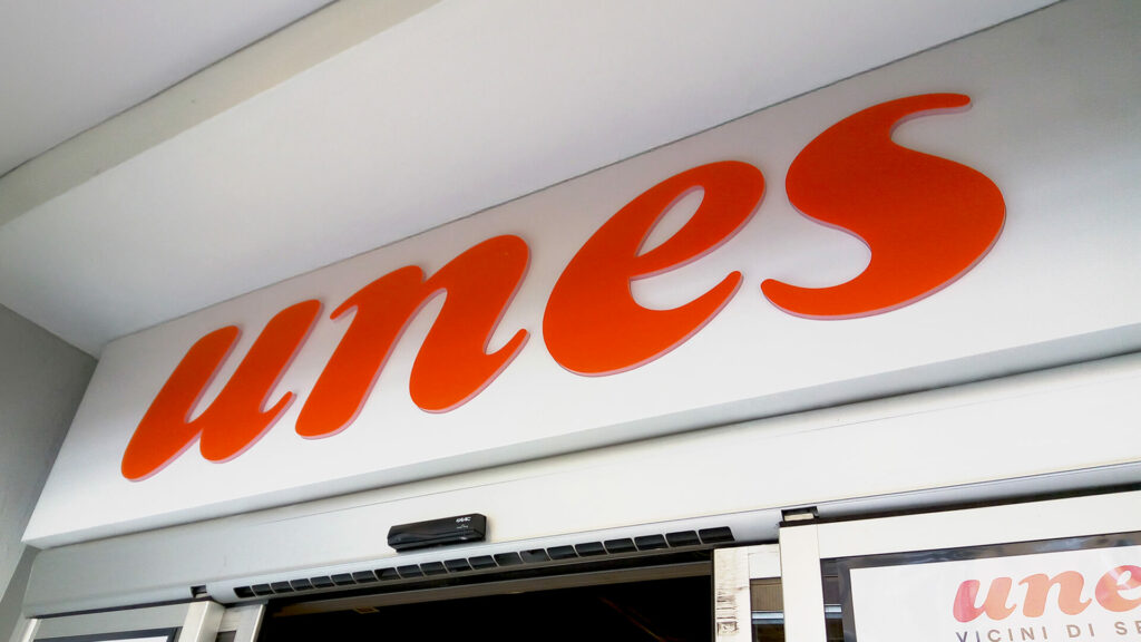 Insegna luminosa arancione del logo Unes applicata su parete bianca all'ingresso