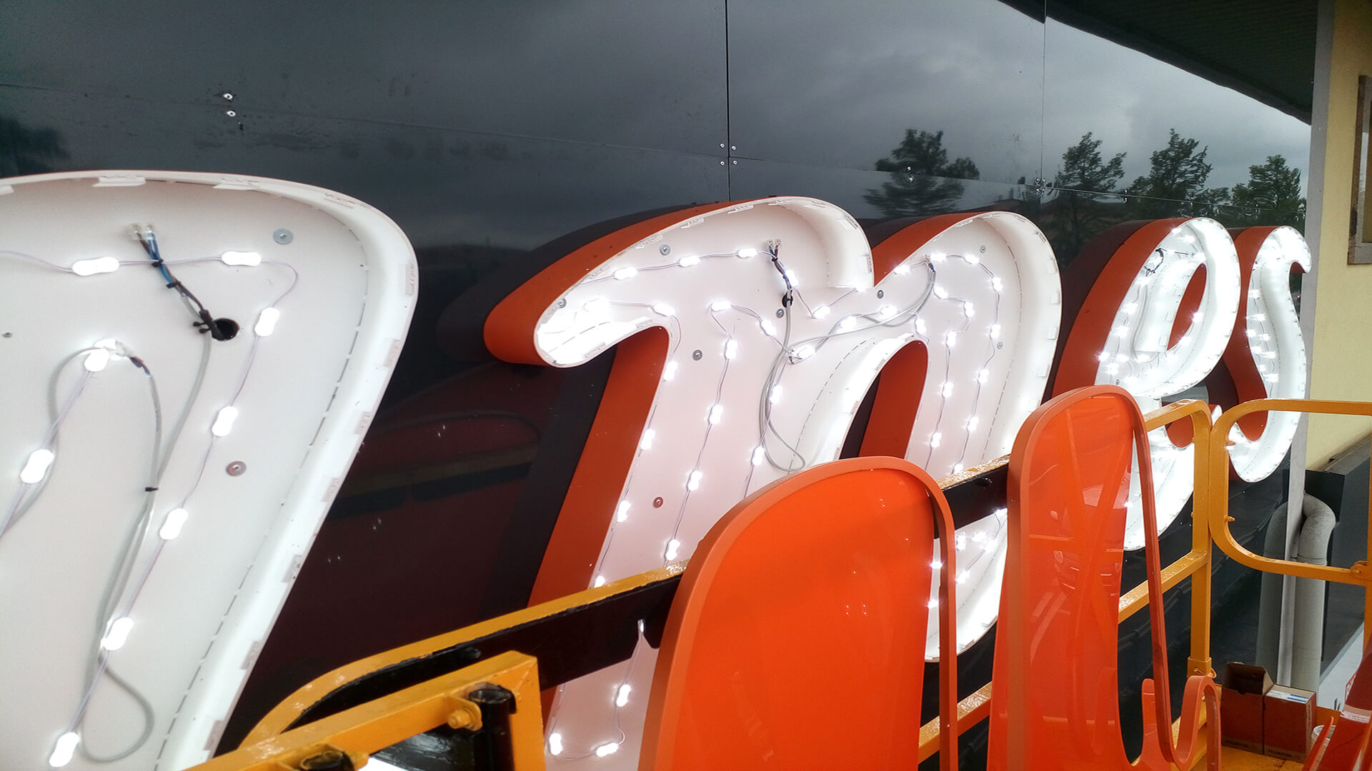 Insegna Unes in fase di lavorazione con moduli LED in vista che illuminano la struttura arancione in rilievo ideale per insegne luminose da esterno